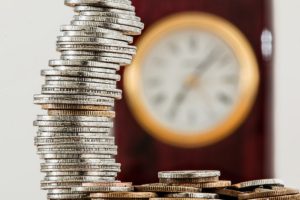 Coins stacked up in front of a blurry clock