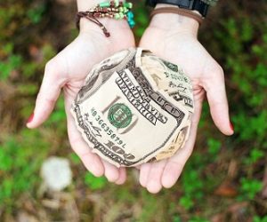 Woman holding ball od 100 dollar bills in her hands